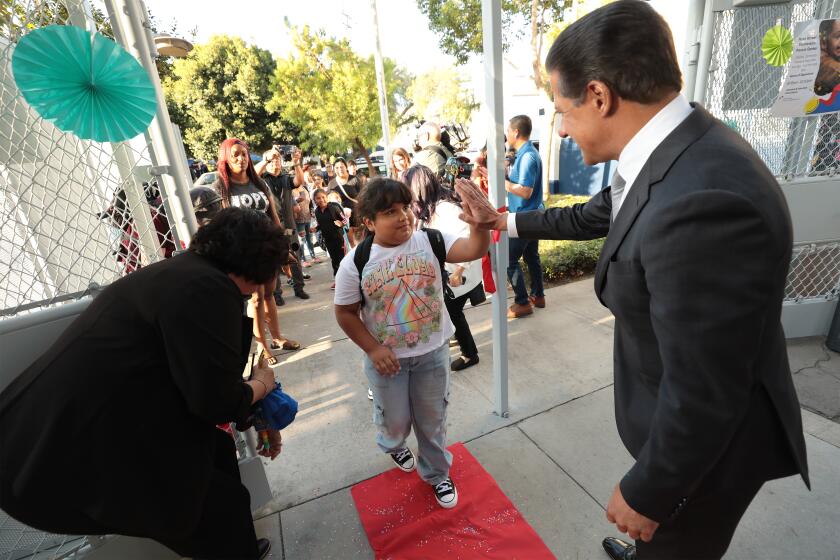 The superintendent high fives a student as he walks into school across a red carpet.