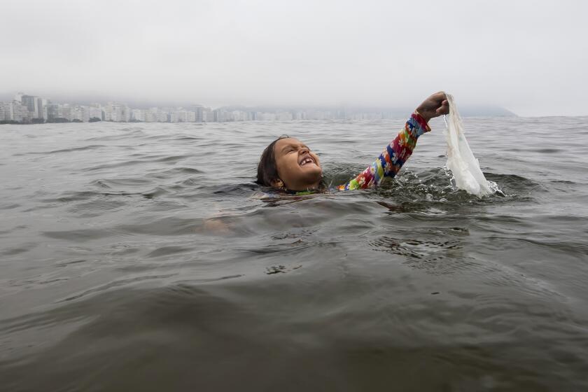 Nina Gomes recovers a discarded plastic bag from ocean waters, near Copacabana beach in Rio de Janeiro, Brazil, March 19, 2024. The seven-year-old Brazilian environmental activist has spent years collecting garbage in the waters of Copacabana beach and teaching conservation methods to other children. (AP Photo/Bruna Prado)