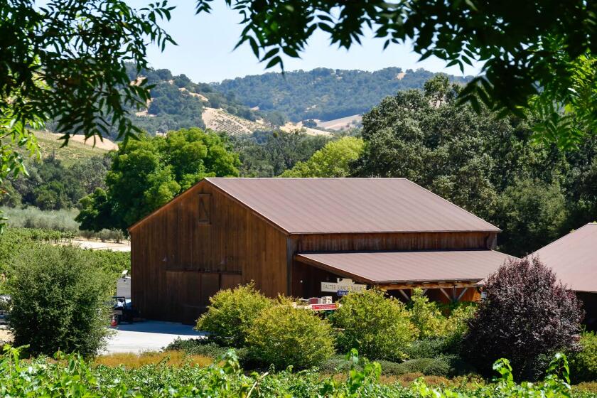 Wooden wine tasting room exterior surrounded by lush trees, shrubs and rolling hills