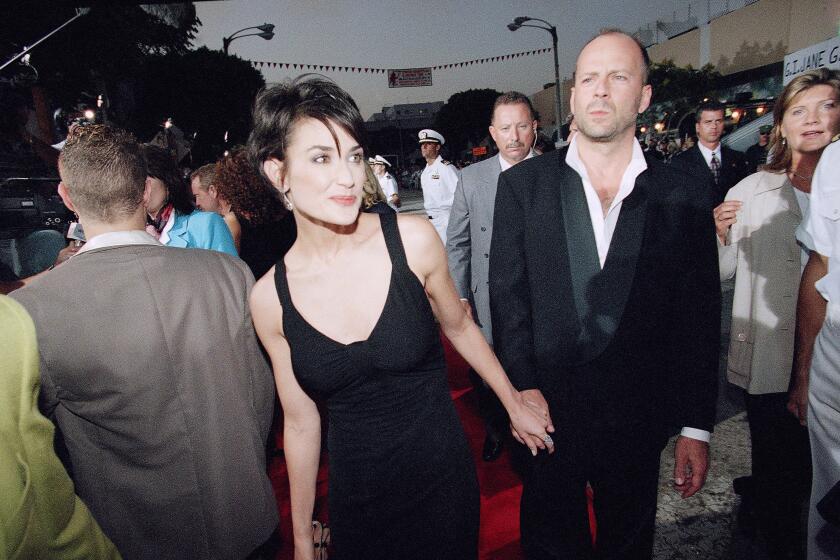 Demi Moore with short hair in a black dress holding hands with Bruce Willis in a suit at a red carpet premiere in Westwood