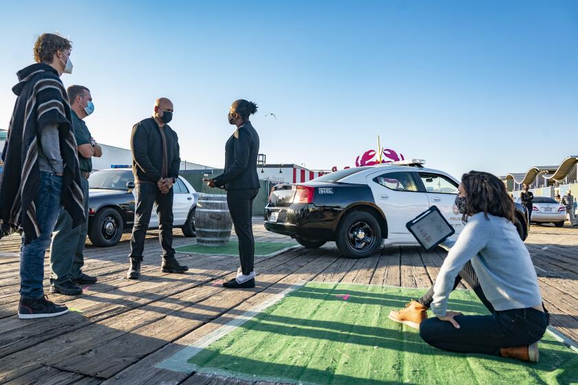 Workers and actors standing on a street next to a police car while filming a TV show