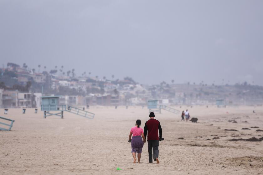 Venice, CA - June 03: A couple walk along the shoreline under cloudy skies on Monday, June 3, 2024 in Venice, CA. (Brian van der Brug / Los Angeles Times)