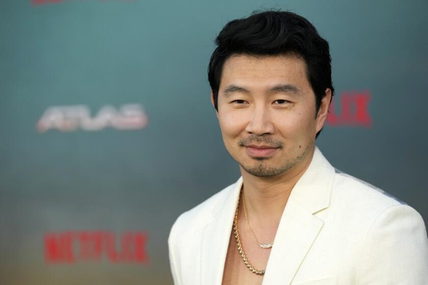 Simu Liu poses in a white suit and gold chain necklaces at the May 2024 Netflix premiere of "Atlas" at the Egyptian Theatre