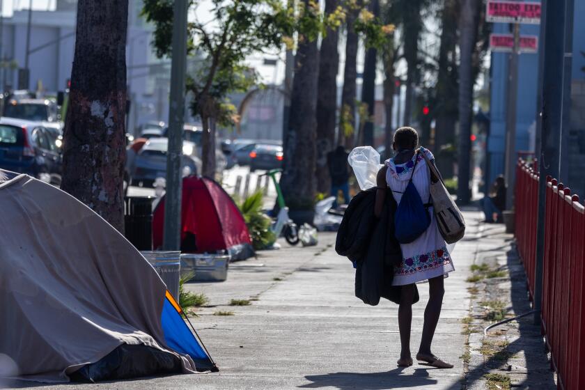 Hollywood, CA - August 15: A homeless woman walks with her belongings as Mayor Karen Bass' Inside Safe program employees along with the Los Angeles Sanitation Bureau clean up homeless encampments along Hollywood Blvd. and Gower Street on Thursday, Aug. 15, 2024 in Hollywood, CA. (Brian van der Brug / Los Angeles Times)